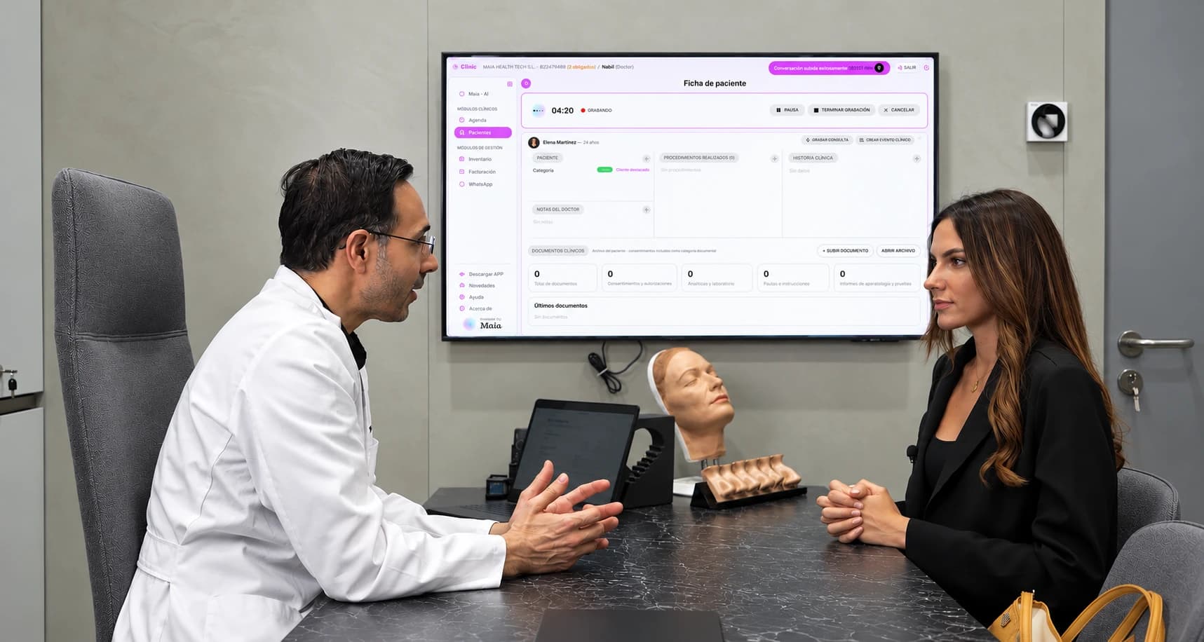 Un médico y una paciente conversan en la consulta mientras Maia graba y rellena la ficha en la pantalla.